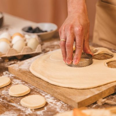 A detailed view of a hand cutting dough using a cookie cutter on a wooden board.