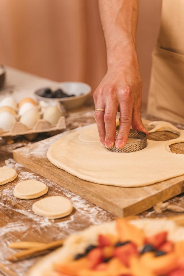 A detailed view of a hand cutting dough using a cookie cutter on a wooden board.