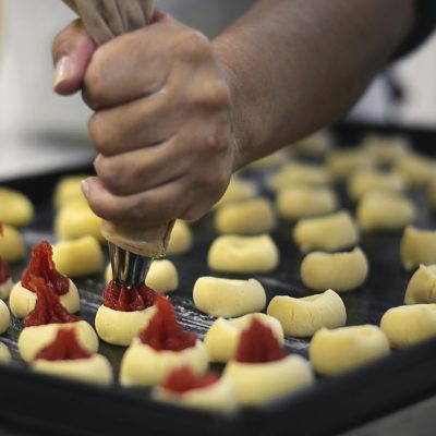 Close-up of a baker using a piping bag to fill pastries with jam, showcasing the preparation process.