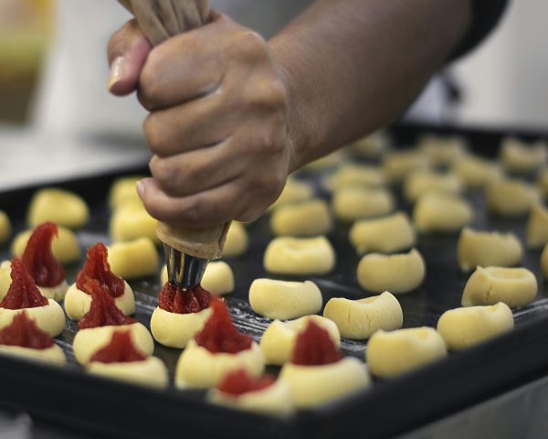 Close-up of a baker using a piping bag to fill pastries with jam, showcasing the preparation process.