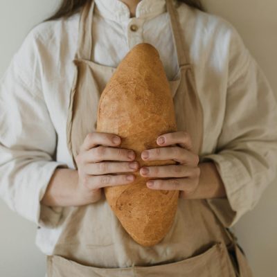 Close-up of a person in an apron holding a freshly baked loaf of bread.