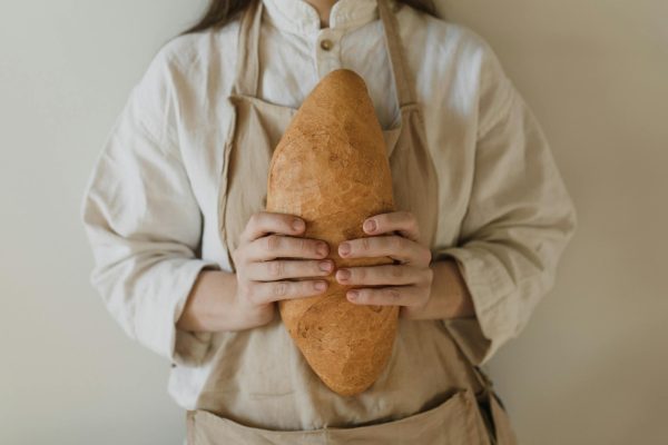 Close-up of a person in an apron holding a freshly baked loaf of bread.