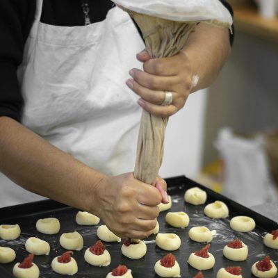 Close-up of hands piping jam into cookie dough in a bakery setup, showcasing pastry preparation.