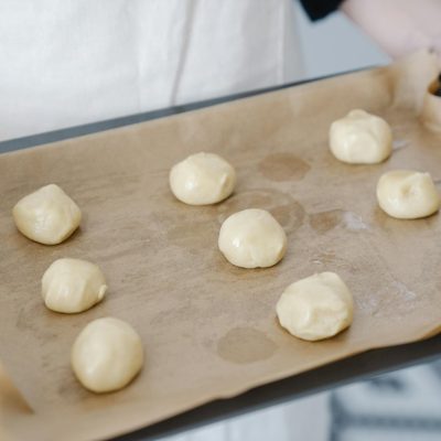 Person holding a baking tray with dough balls ready for baking.