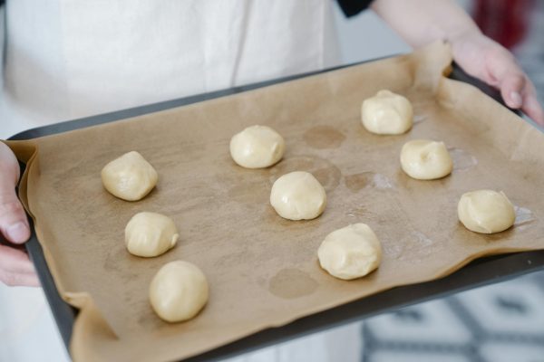 Person holding a baking tray with dough balls ready for baking.