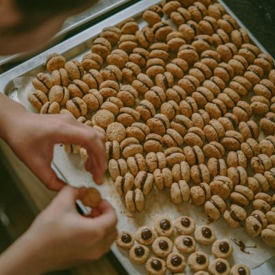 Person preparing a large batch of cookies on a tray, showing attention to detail in a cozy kitchen setting.