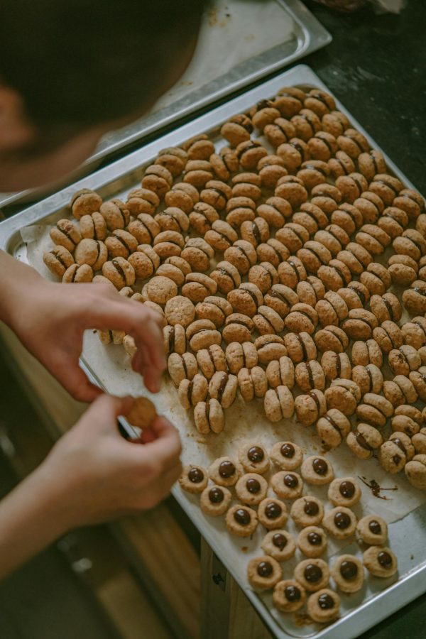 Person preparing a large batch of cookies on a tray, showing attention to detail in a cozy kitchen setting.